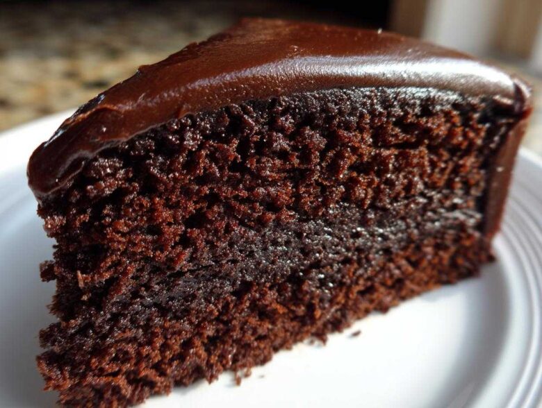 Close-up of a rich, moist slice of chocolate cake recipe topped with glossy dark chocolate frosting.
