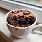 Close-up of a rich, moist chocolate mug cake with melted chocolate pooling at the bottom and chocolate chips on top.