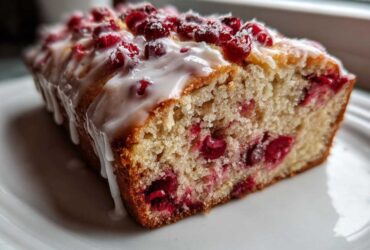 A close-up of a slice of moist cranberry orange bread topped with white glaze and fresh cranberries.