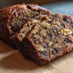 Close-up of sliced date nut bread showing moist texture, dates, and walnuts on a wooden board.