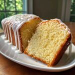 A slice cut from a loaf of moist lemon pound cake covered in dripping white glaze.