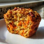 Close-up of a morning glory muffins cut in half, showing shredded carrots, nuts, and moist texture.