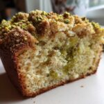 A close-up view of a slice of moist pistachio coffee cake showing the crumb texture and pistachio topping.