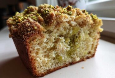 A close-up view of a slice of moist pistachio coffee cake showing the crumb texture and pistachio topping.