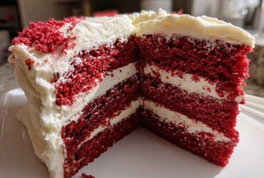 Close-up of a moist slice of red velvet cake showing three vibrant red layers separated by thick white cream cheese frosting.