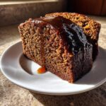 Close-up of a moist slice of dark rum cake recipe topped with a thick, dripping caramel glaze.