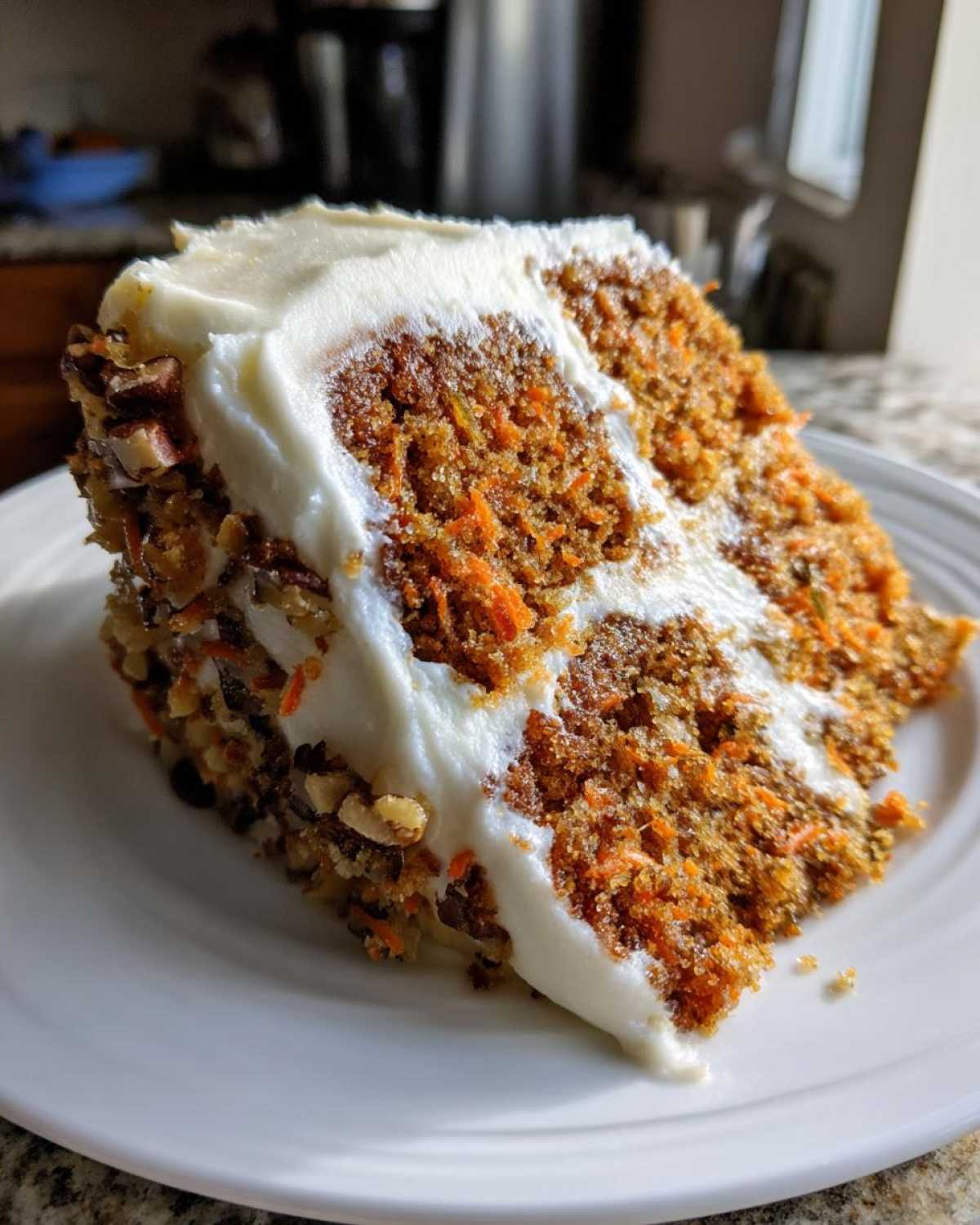 Close-up of a thick slice of moist carrot cake recipe with visible shredded carrots and nuts, topped with cream cheese frosting.