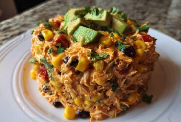 A molded serving of creamy, orange-hued southwest chicken salad mixed with corn and black beans, topped with avocado slices.