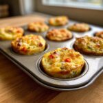 Close-up of fluffy muffin tin egg bites with cheese and peppers baked in a metal muffin pan.