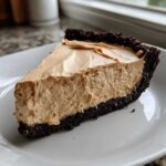 A thick slice of no-bake peanut butter pie with a creamy filling and dark chocolate crust, served on a white plate.
