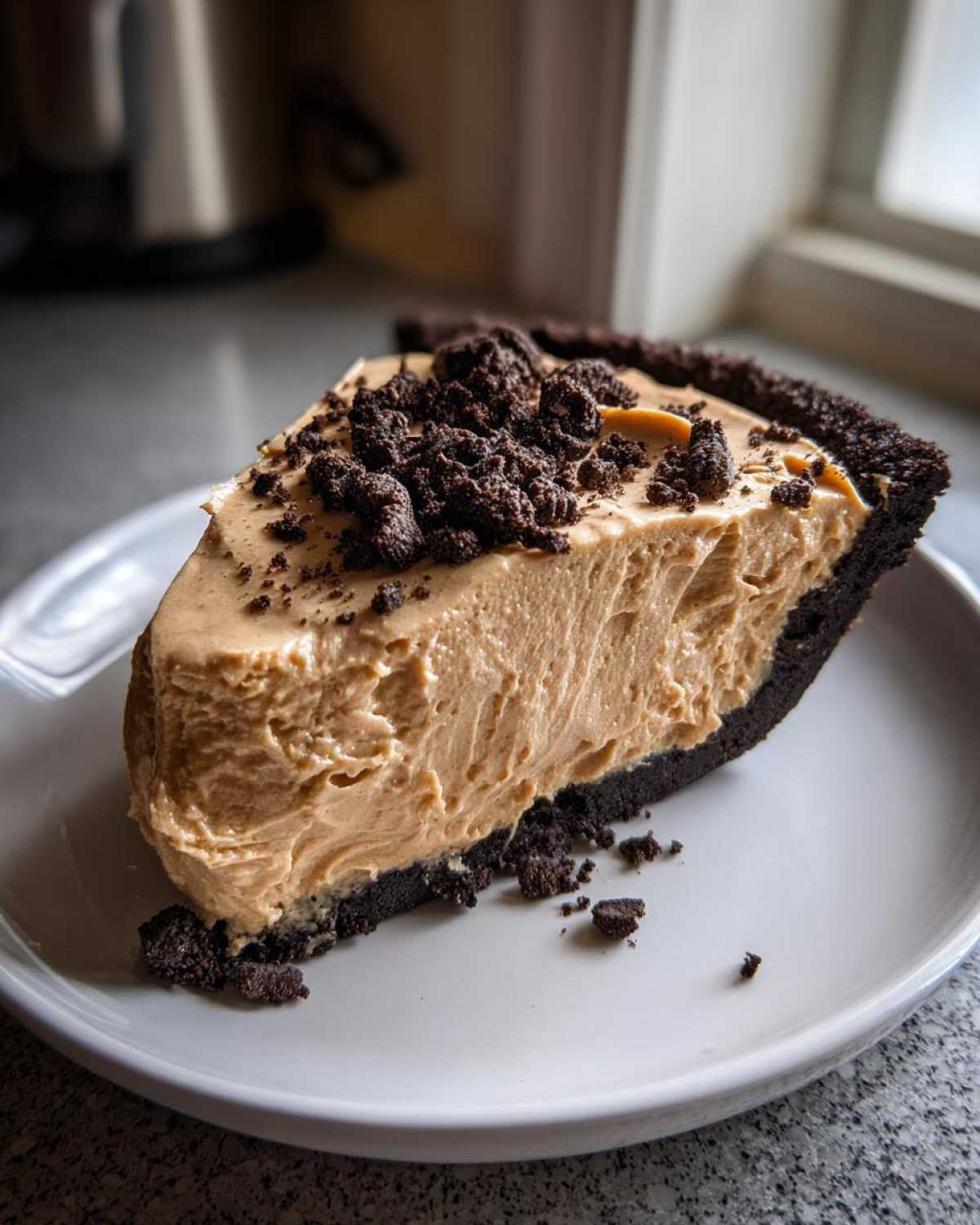 A thick slice of no-bake peanut butter pie with a dark chocolate crust, topped with chocolate cookie crumbles.