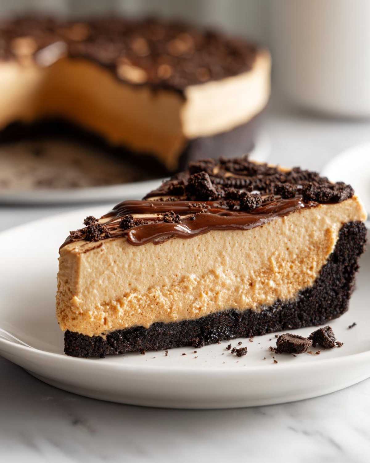 A generous slice of no-bake peanut butter pie featuring a thick peanut butter filling and dark chocolate crust, drizzled with fudge.