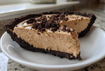 A thick slice of creamy no-bake peanut butter pie with a dark chocolate crust and crumb topping on a white plate.
