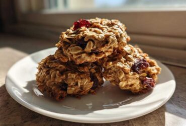 Three healthy oatmeal breakfast cookie treats stacked on a white plate, featuring visible oats and dried cranberries.