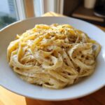 Close-up of fettuccine pasta coated in rich, creamy Olive Garden Alfredo Sauce and topped with black pepper.
