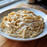 A close-up of fettuccine pasta generously coated in creamy Olive Garden Alfredo sauce in a white bowl.