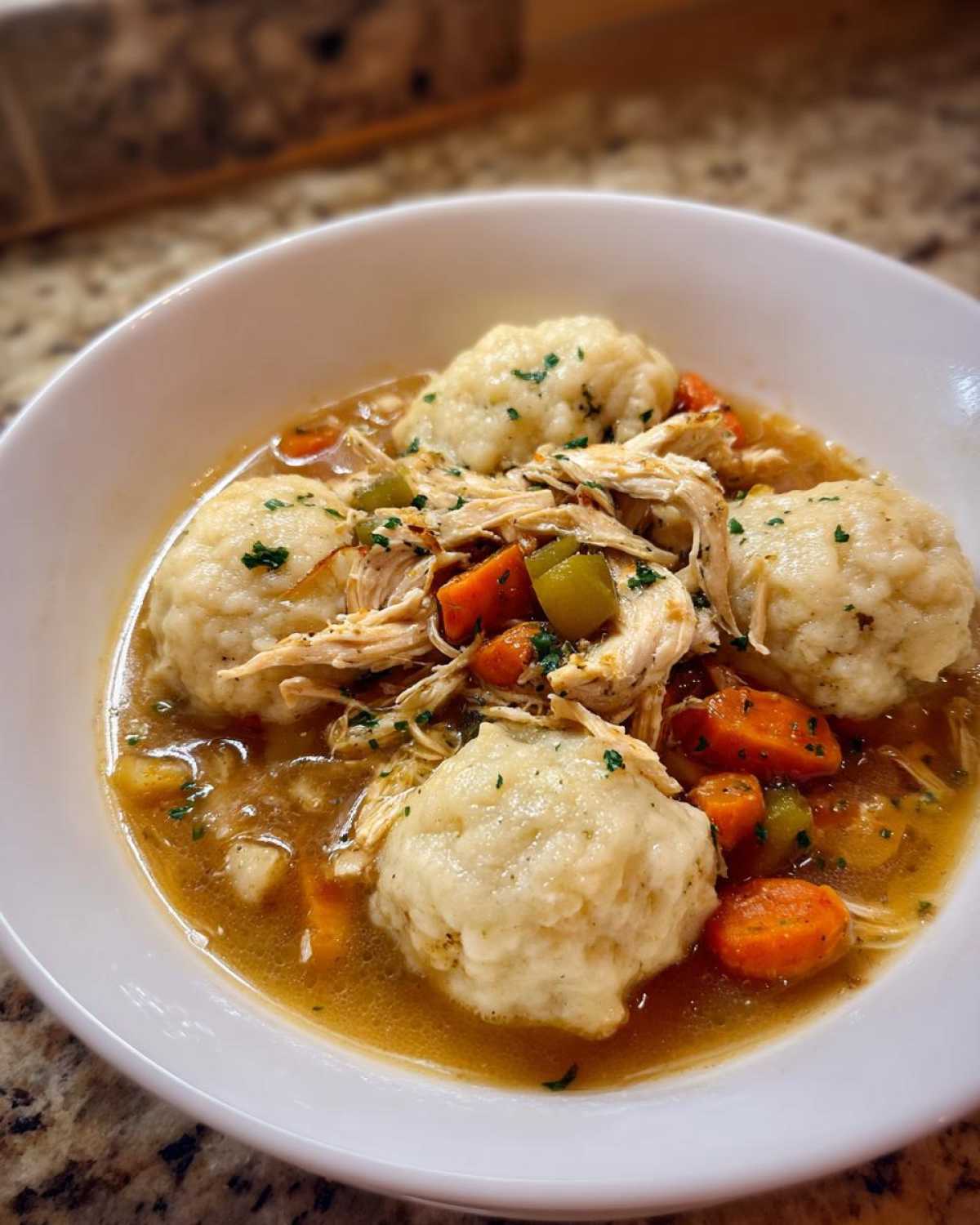 Close-up of a white bowl filled with rich broth, shredded chicken, carrots, and fluffy dumplings from the chicken and dumpling recipe.