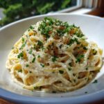 Close-up of creamy pasta coated in a rich sauce, topped with grated cheese, black pepper, and fresh parsley, showcasing the garlic parmesan flavor.