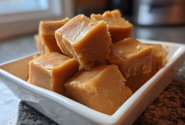 Close-up of rich, light brown squares of melt-in-mouth penuche fudge stacked in a small white dish.