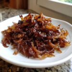 A mound of deeply browned, glossy caramelized onions piled high on a small white dish.