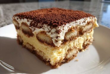 A close-up view of a perfect slice of homemade tiramisu recipe, layered with cream and dusted heavily with cocoa powder.