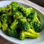 Close-up of vibrant green, perfectly cooked steamed broccoli florets seasoned in a white serving dish.