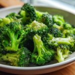 Close-up of bright green, perfectly steamed broccoli florets seasoned with pepper and salt in a light gray bowl.
