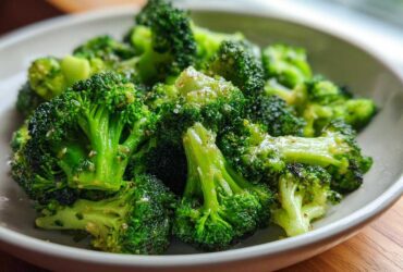 Close-up of bright green, perfectly steamed broccoli florets seasoned with pepper and salt in a light gray bowl.