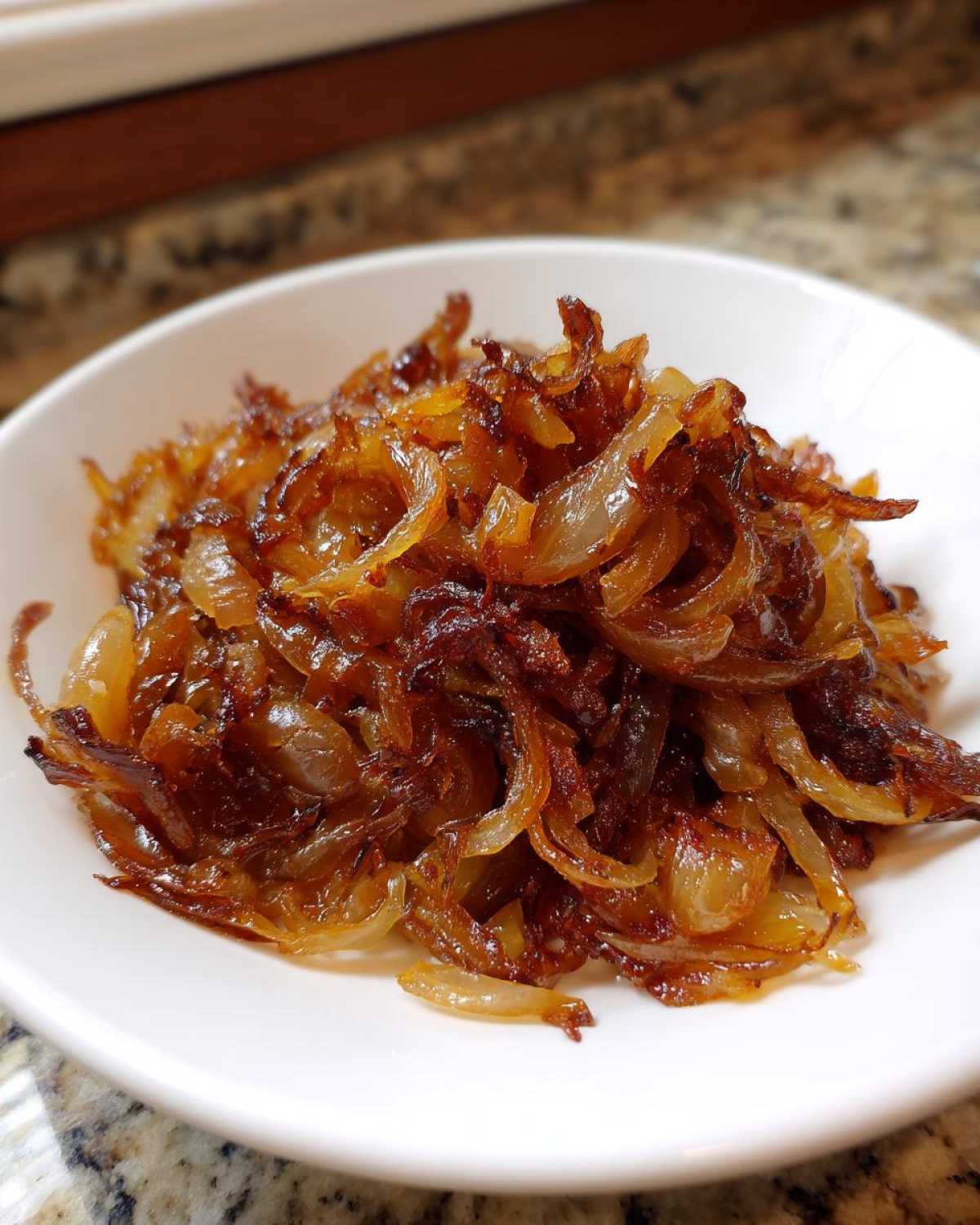 A close-up of deeply browned, sweet caramelized onions piled high in a small white bowl.