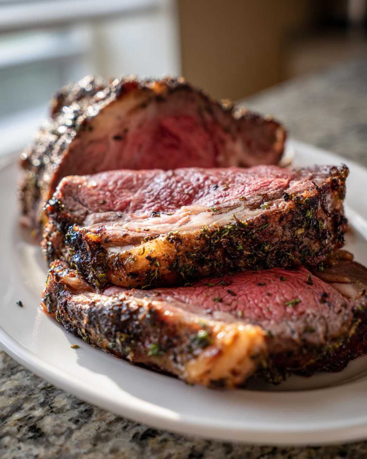 Close-up of thick, medium-rare slices from a perfectly seasoned prime rib recipe on a white platter.