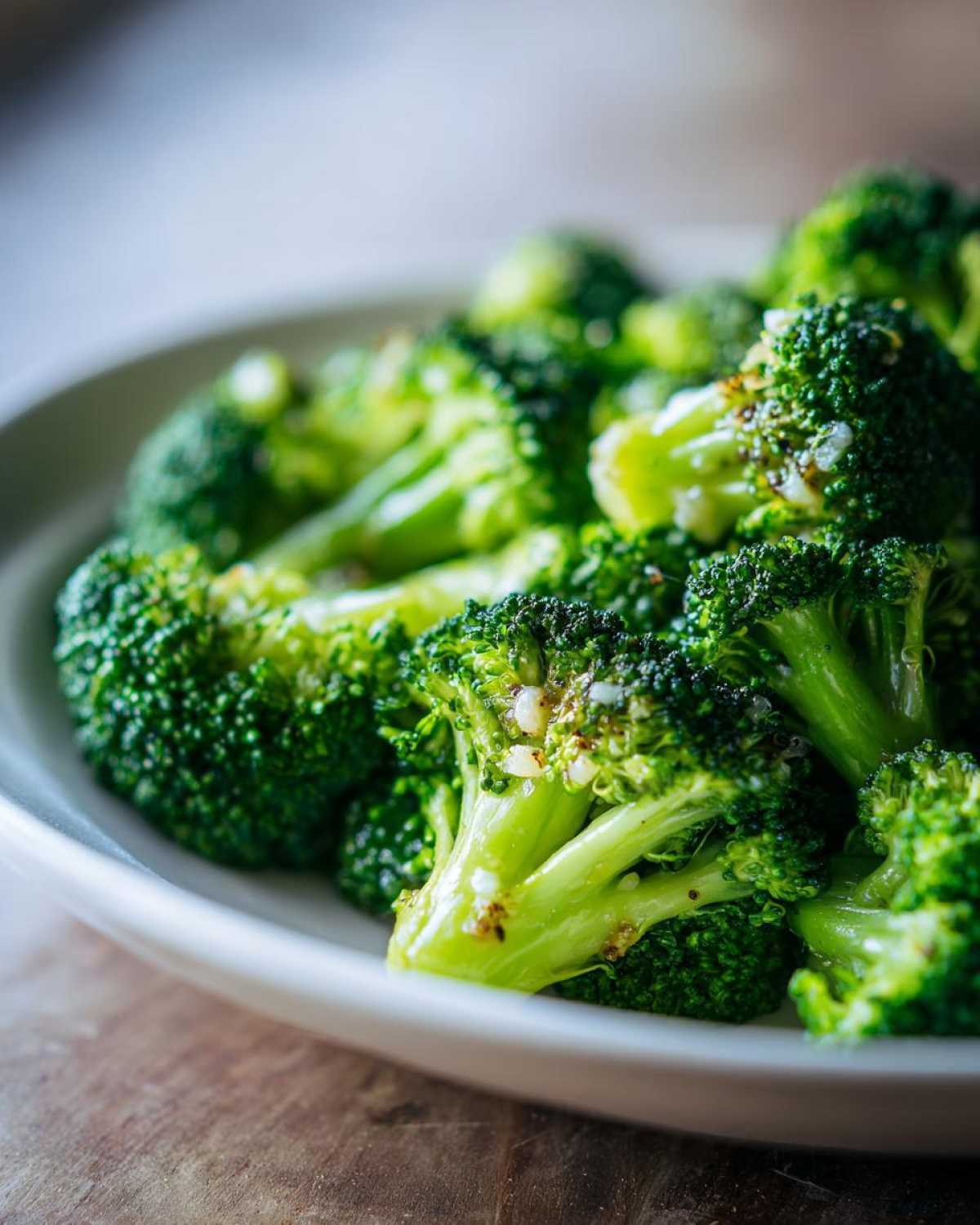 Close-up of bright green steamed broccoli florets seasoned with garlic bits in a white bowl.