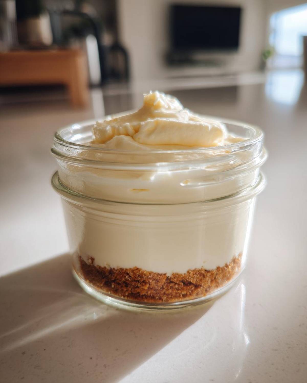 A single serving of layered Protein Cheesecake in a small glass jar with a graham cracker crust.