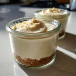 Two individual servings of creamy Protein Cheesecake layered over a graham cracker crust in small glass jars.