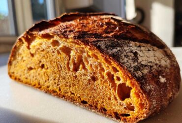 Close-up of the vibrant orange crumb and dark crust of a freshly baked pumpkin sourdough loaf.