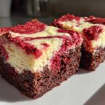 Two rich, fudgy red velvet cheesecake brownies squares with a marbled red and cream cheese topping.