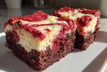 Two rich, fudgy red velvet cheesecake brownies squares with a marbled red and cream cheese topping.
