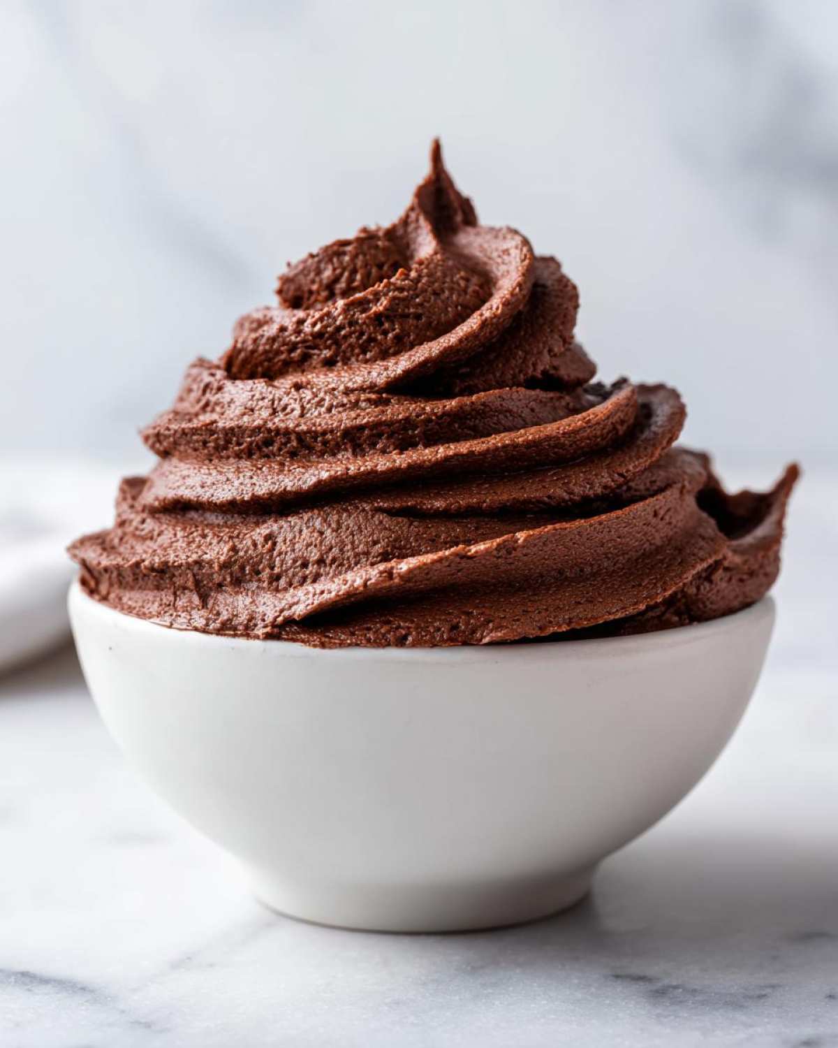 A perfectly piped swirl of rich, dark chocolate frosting mounded high in a small white bowl.