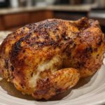 A beautifully roasted whole chicken with deeply browned, crispy skin resting on a white plate.