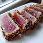 Close-up of perfectly seared ahi tuna slices, crusted with black and white sesame seeds, showing a rare pink center.