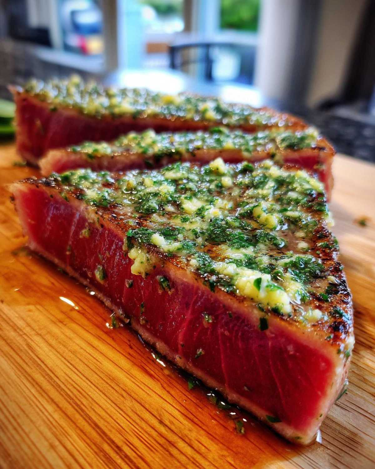 Close-up of a perfectly seared, rare tuna steak sliced and topped with a bright green herb and garlic butter.