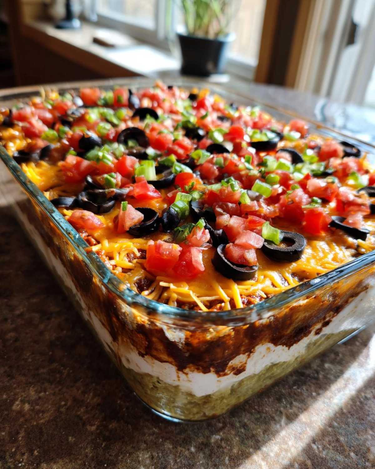A rectangular glass dish filled with a colorful Seven layer dip, topped with cheese, olives, tomatoes, and green onions.