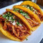 Three delicious chicken tacos filled with saucy shredded chicken, topped with diced white onion and fresh cilantro.