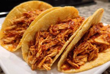 Close-up of three delicious chicken tacos filled with shredded chicken coated in a rich red sauce.