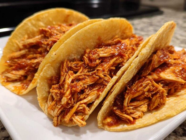 Close-up of three delicious chicken tacos filled with shredded chicken coated in a rich red sauce.