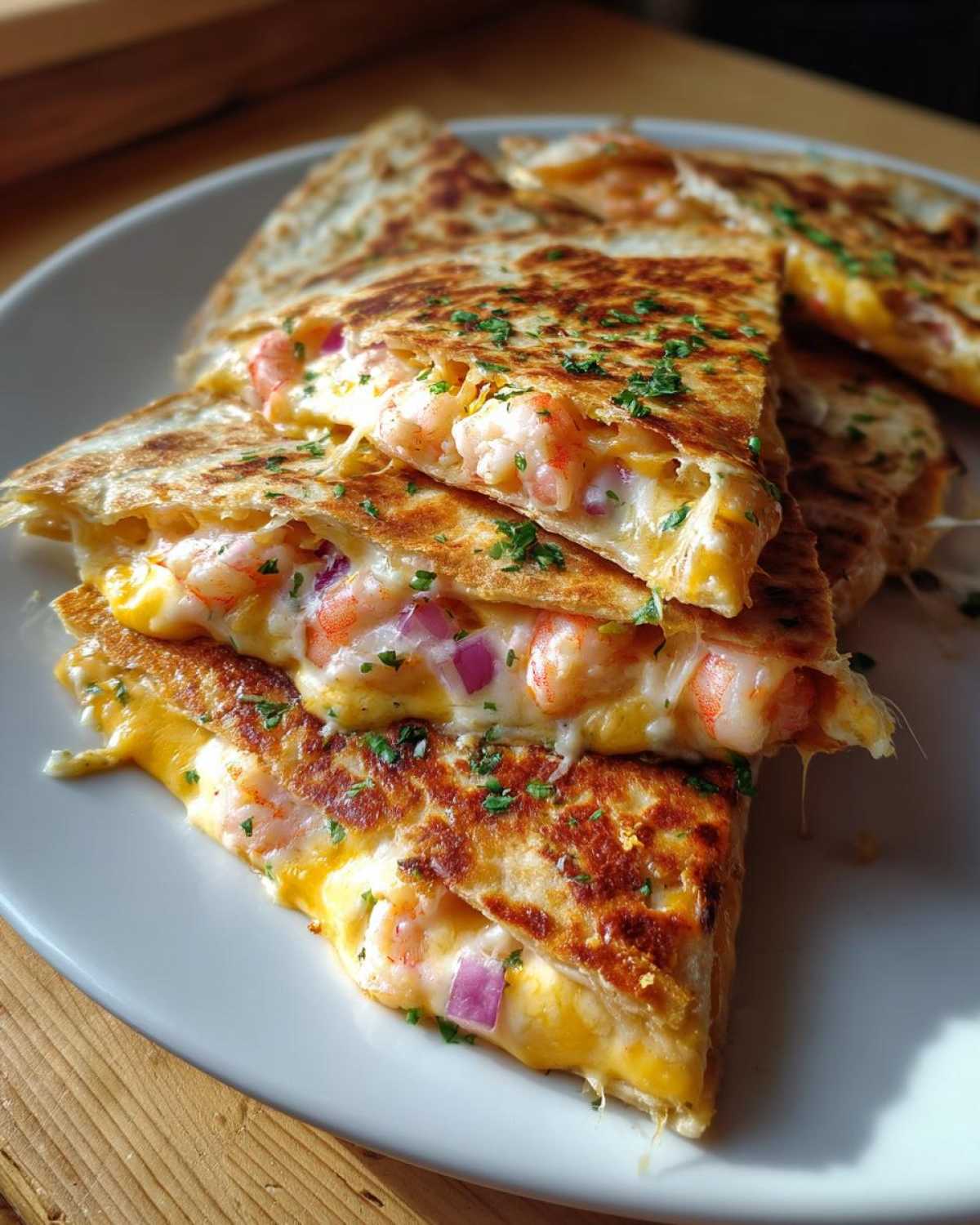 Close-up of stacked, grilled shrimp quesadilla slices oozing melted cheese, shrimp, and red onion, topped with parsley.