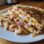 Close-up of two wedges of a golden-brown shrimp quesadilla overflowing with melted cheese, shrimp, and peppers.