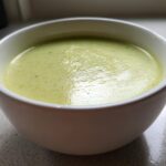 Close-up of a bowl of silky, pale green leek soup resting on a light countertop.