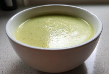 Close-up of a bowl of silky, pale green leek soup resting on a light countertop.