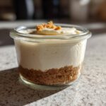A single serving Protein Cheesecake layered in a small glass jar with a graham cracker crust and crumb topping.