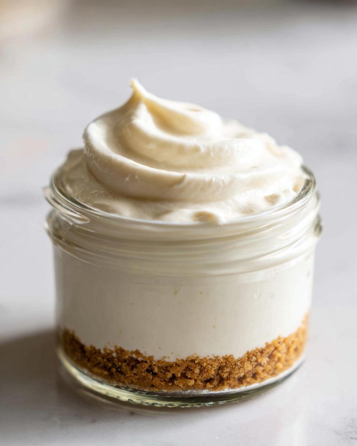 Close-up of a single serving Protein Cheesecake in a small glass jar with a graham cracker crust and swirled topping.